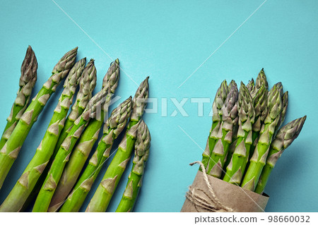 An edible, raw stems of asparagus on blue background. An edible, raw stems of asparagus on blue background. 98660032