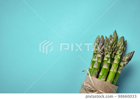 An edible, raw stems of asparagus on blue background. An edible, raw stems of asparagus on blue background. 98660033