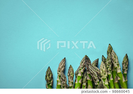 An edible, raw stems of asparagus on blue background. 98660045