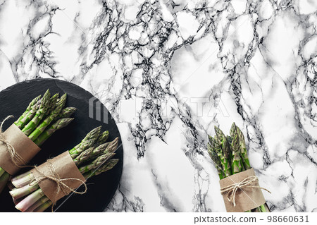 An edible, raw stems of asparagus on a marble background. An edible, raw stems of asparagus on a marble background. 98660631