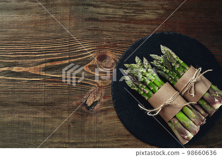 An edible, raw stems of asparagus on a wooden background. An edible, raw stems of asparagus on a wooden background. 98660636