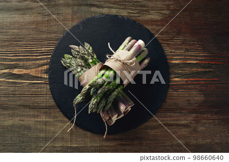 An edible, raw stems of asparagus on a wooden background. An edible, raw stems of asparagus on a wooden background. 98660640