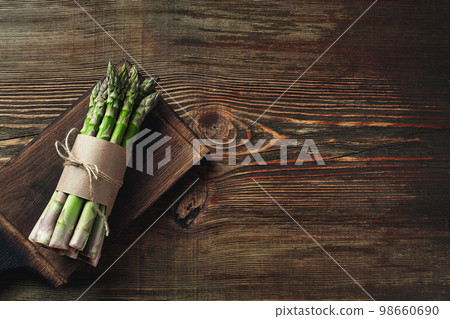 An edible, raw stems of asparagus on a wooden background. 98660690