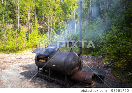 Huge wood smoker stands on the edge of the forest on a sunny day Huge wood smoker stands on the edge of the forest on a sunny day 98661720