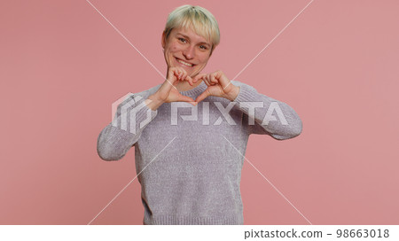 Smiling pretty woman makes heart gesture demonstrates love sign expresses good feelings and sympathy Smiling pretty woman makes heart gesture demonstrates love sign expresses good feelings and sympathy 98663018