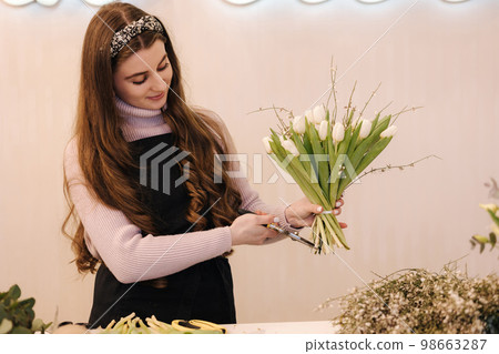 Flowers delivery shop. Florist creating order, making spring bouquet. Female make bouquet using tulips Flowers delivery shop. Florist creating order, making spring bouquet. Female make bouquet using tulips 98663287