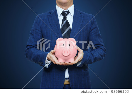 Businessman in suit is holding piggy bank. Businessman holding pig money box Businessman in suit is holding piggy bank. Businessman holding pig money box 98666303