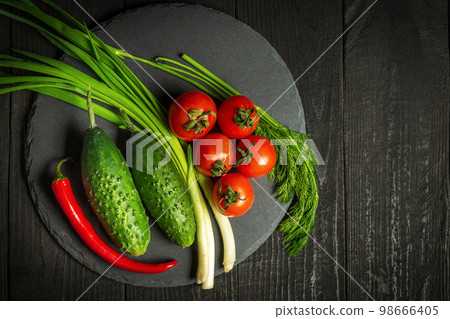 Big set for fresh vegetable salad. Red tomatoes and green young onions with cucumber on a vintage brown plate Big set for fresh vegetable salad. Red tomatoes and green young onions with cucumber on a vintage brown plate 98666405