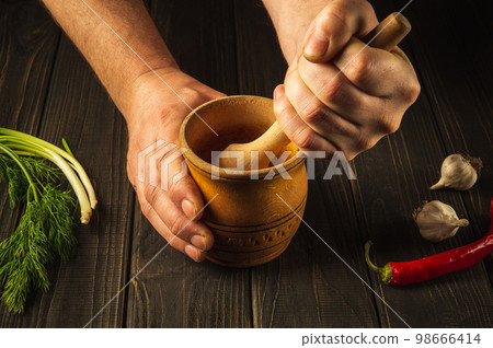 The chef crushing a blending red pepper in a wooden pestle and mortar. Cooking a national. Close-up of a cook hands while working. Peasant foods The chef crushing a blending red pepper in a wooden pestle and mortar. Cooking a national. Close-up of a cook hands while working. Peasant foods 98666414