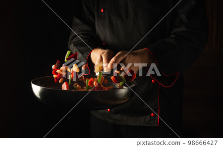 Cooking fresh vegetables in a frying pan by a chef for a vegetarian diet. Space for advertising a hotel or restaurant Cooking fresh vegetables in a frying pan by a chef for a vegetarian diet. Space for advertising a hotel or restaurant 98666427