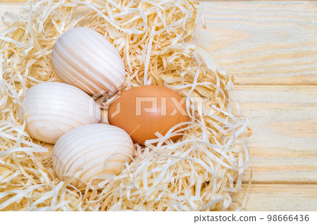 Egg and three wooden eggs in a nest with wood shavings. Idea for celebrating Easter Egg and three wooden eggs in a nest with wood shavings. Idea for celebrating Easter 98666436