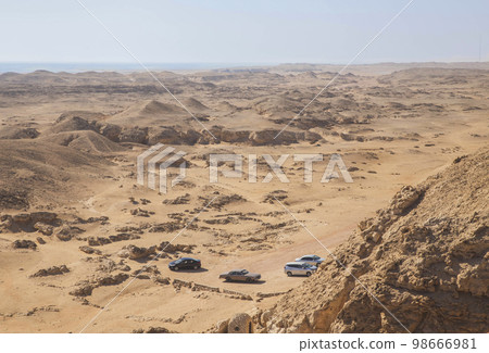 Four cars are parked in the desert. The sea on the horizon Four cars are parked in the desert. The sea on the horizon 98666981