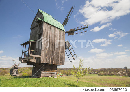 Antique wooden windmills on a hill near the village. Rural landscape Antique wooden windmills on a hill near the village. Rural landscape 98667020