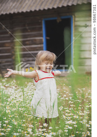 charming baby in an embroidered dress enjoys flowers near a wooden hut charming baby in an embroidered dress enjoys flowers near a wooden hut 98667381