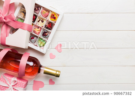 Bottle of red wine on colored background for Valentine Day with gift and chocolate. Heart shaped with gift box of chocolates top view with copy space Bottle of red wine on colored background for Valentine Day with gift and chocolate. Heart shaped with gift box of chocolates top view with copy space 98667382