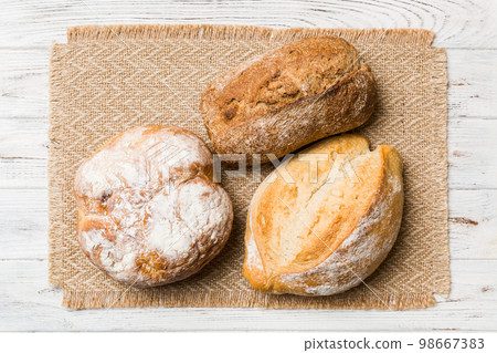 Assortment of freshly baked bread with napkin on rustic table top view. Healthy unleavened bread. French bread Assortment of freshly baked bread with napkin on rustic table top view. Healthy unleavened bread. French bread 98667383