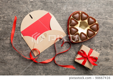 Envelope on colored background for Valentine Day with gift box and chocolate. Heart shaped with gift box of chocolates top view with copy space 98667416