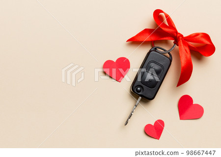 Car key with a red bow and a heart on Colored table. Giving present or gift for valentine day or christmas, Top view with copy space Car key with a red bow and a heart on Colored table. Giving present or gift for valentine day or christmas, Top view with copy space 98667447