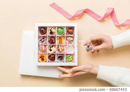 Female hands with delicious candies in box on color background 98667453