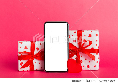 mobile phone with blank screen on colored background with hearts, calendar and gift box, valentine day concept perspertive view flat lay mobile phone with blank screen on colored background with hearts, calendar and gift box, valentine day concept perspertive view flat lay 98667506
