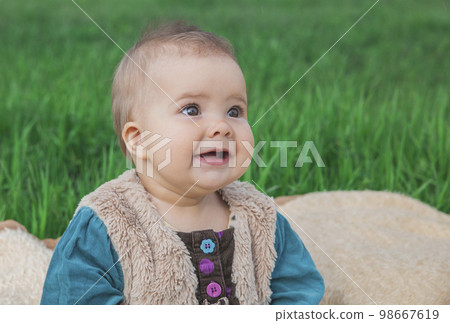 toothless baby in a multi-colored dress sitting on a bedspread on lawn toothless baby in a multi-colored dress sitting on a bedspread on lawn 98667619