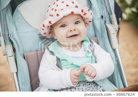 baby in hat smiles toothlessly sitting in a blue stroller baby in hat smiles toothlessly sitting in a blue stroller 98667624