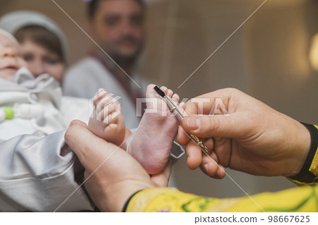 The priest performs the ceremony of anointing the baby The priest performs the ceremony of anointing the baby 98667625