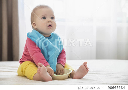 charming baby in bib with a plate waiting for lunch 98667684