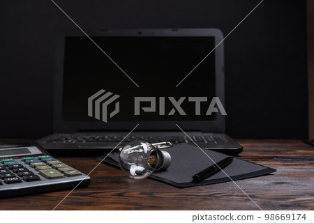 Ordinary incandescent lamp and office. Light bulb and calculator. Glass lamp on the table. 98669174