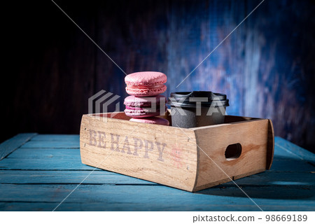 Macaroons and coffee in a wooden tray. Multicolored macaroons and coffee in a wooden box. Colored background. 98669189