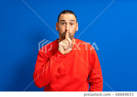 Serious handsome bearded hispanic man puts his index finger to his lips, tries to keep conspiracy, looks aside and says: Shh, be quiet please. Isolated shot of attractive man shows silence sign. Serious handsome bearded hispanic man puts his index finger to his lips, tries to keep conspiracy, looks aside and says: Shh, be quiet please. Isolated shot of attractive man shows silence sign. 98669655