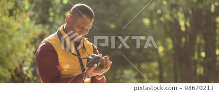 Banner african american guy photographer taking picture with photo camera on city green park copy space and place for text - leisure activity, diversity and hobby concept 98670211