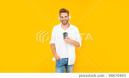 cheerful guy with bristle listen music drink coffee on yellow background, modern device 98670403