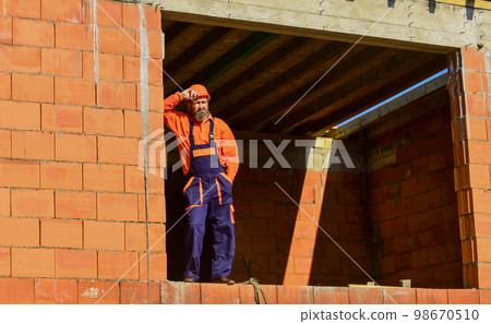 Daily routine at construction. Well done. Repairman tired builder relaxing at construction site. Builder smoking cigarette. Break and relax. Bearded man in engineer uniform and hard hat. Regular day Daily routine at construction. Well done. Repairman tired builder relaxing at construction site. Builder smoking cigarette. Break and relax. Bearded man in engineer uniform and hard hat. Regular day 98670510