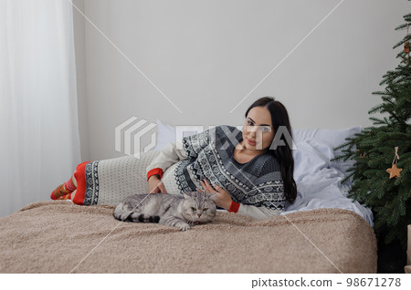 Beautiful young woman lies with a gray cat on the bed 98671278