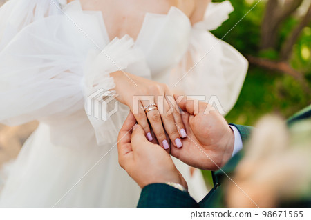 a man's hand holds a woman's hand with a wedding ring on her finger.  98671565