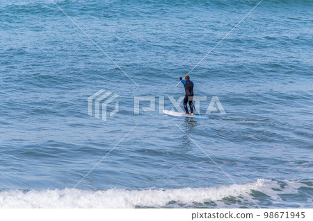 Longboards are very stable boards that are easy to lay on, sit on, paddle on, hit the waves and ride on. They with round nose and tale. In distance A man with a paddle he 98671945
