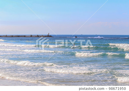 Longboards are very stable boards that are easy to lay on, sit on, paddle on, hit the waves and ride on. They with round nose and tale. In distance A man with a paddle he 98671950