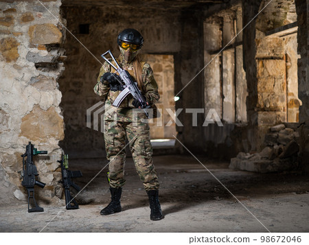 A woman in an army uniform holds a firearm in an abandoned building. 98672046