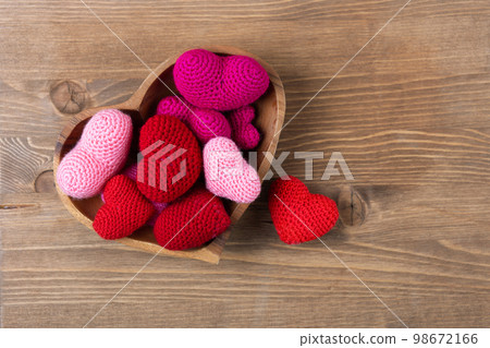 Multicolored pink knitted hearts in a wooden bowl in the shape of a heart on a wooden background. Happy Valentine's Day, Mother's Day and birthday greeting card. Multicolored pink knitted hearts in a wooden bowl in the shape of a heart on a wooden background. Happy Valentine's Day, Mother's Day and birthday greeting card. 98672166