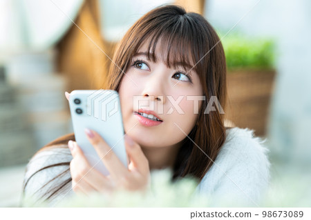 一名躺下並使用智能手機的年輕女子 98673089