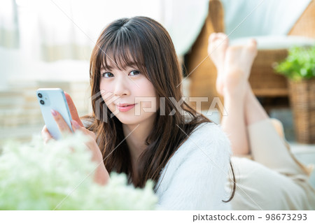 A young woman lying down and using a smartphone A young woman lying down and using a smartphone 98673293