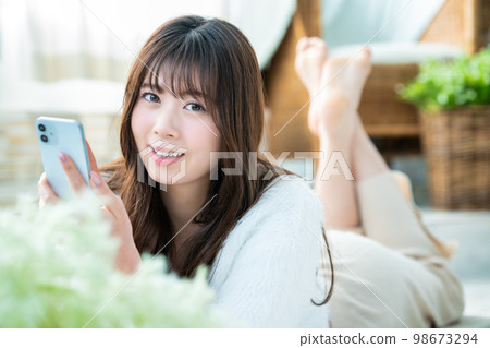 A young woman lying down and using a smartphone A young woman lying down and using a smartphone 98673294