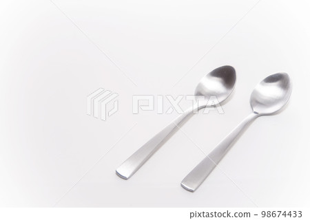Two silver spoons lined up on a white table 98674433