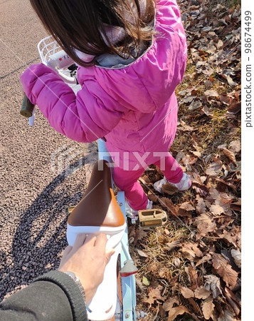 A parent's hand supporting a child from behind as they practice riding a bicycle. A parent's hand supporting a child from behind as they practice riding a bicycle. 98674499