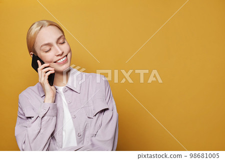 Woman talking on phone against vivid yellow studio wall background 98681005