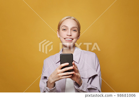 Portrait of a happy businesswoman using mobile phone and smiling against colorful yellow studio  98681006