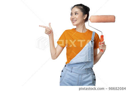 Asian young housewife holding a roller paint brush and pointing something Asian young housewife holding a roller paint brush and pointing something 98682084