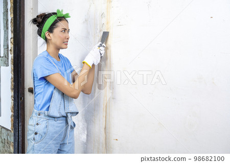Asian young housewife in glove using a paint scraper 98682100