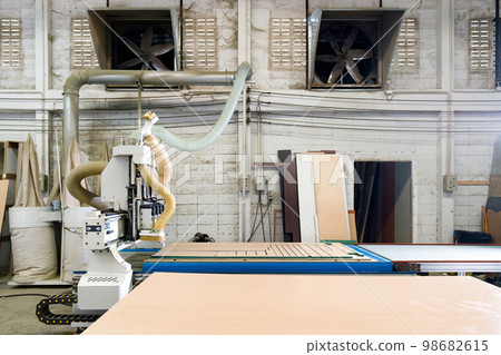 Working table fully loaded with plywood in industrial factory producing wooden furniture parts. An exhaust fans are on lightweight concrete brick wall in the background. Working table fully loaded with plywood in industrial factory producing wooden furniture parts. An exhaust fans are on lightweight concrete brick wall in the background. 98682615